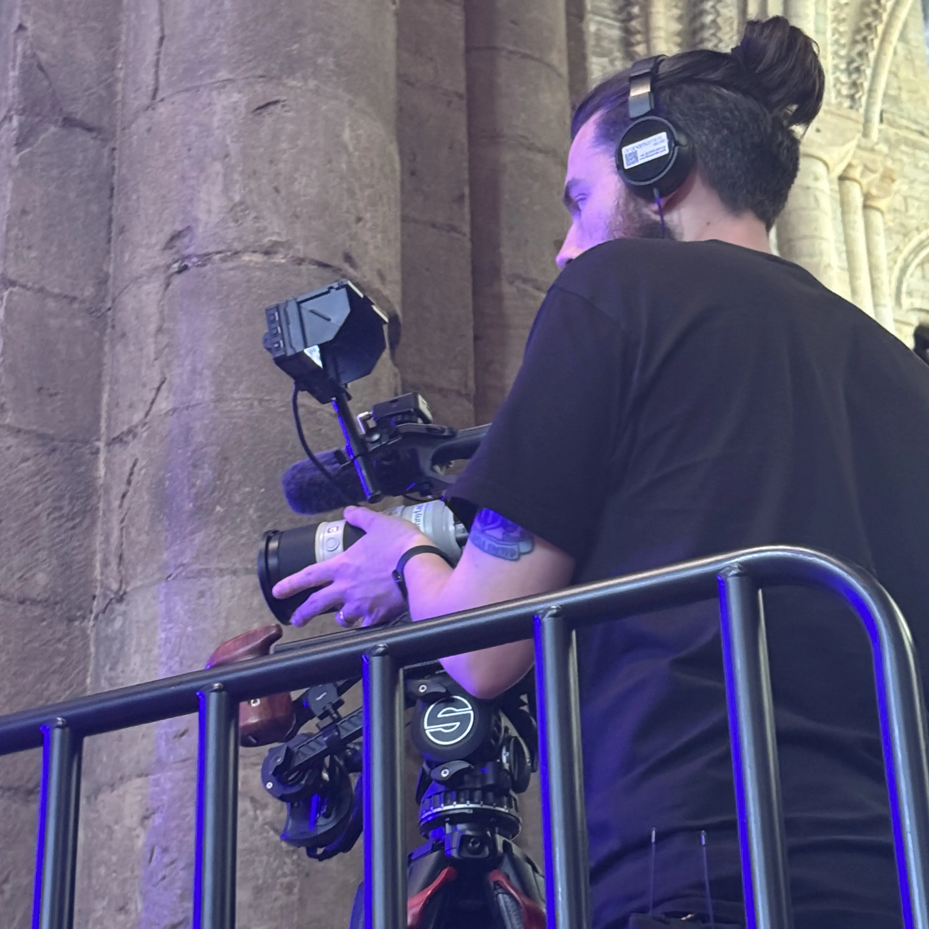 A camera operator with headphones filming on a tripod inside a cathedral